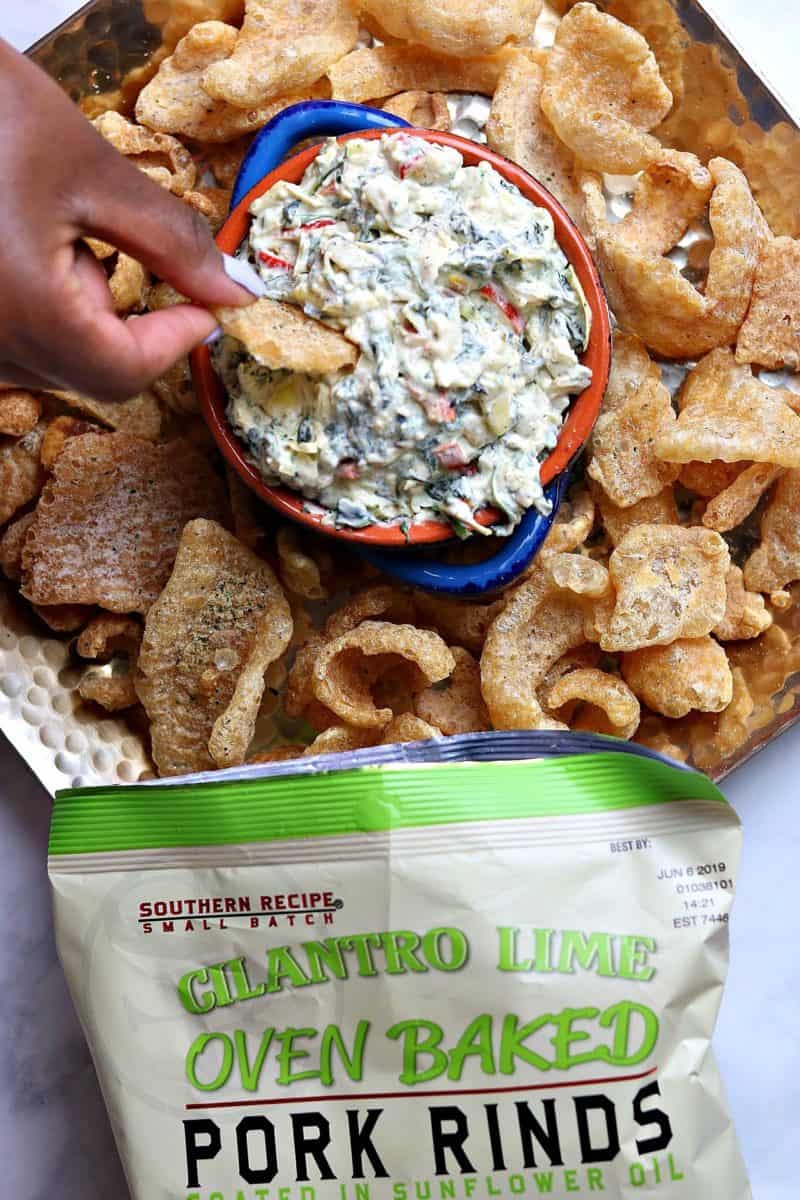 A bowl of Creamy Kale Artichoke Dip on a bed of Cilantro Lime Pork Rind.
