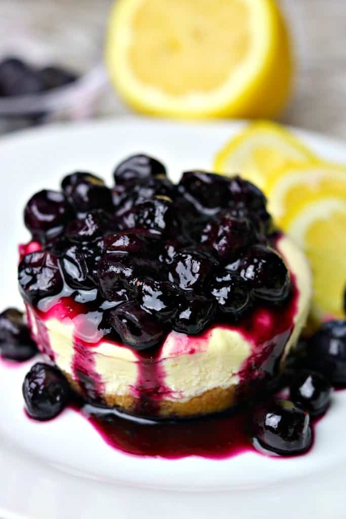 a close-up of gluten-free Lemon Blueberry Cheesecake on a white plate with lemon slices and blueberry sauce