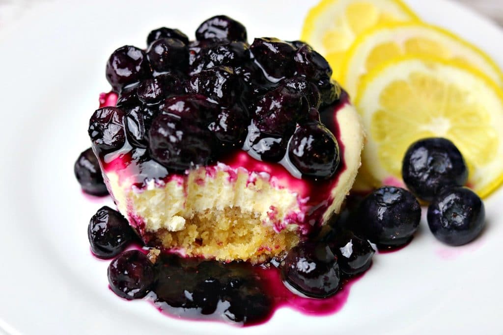 a close-up of sliced Keto Lemon Blueberry Cheesecake on a white plate with lemon slices