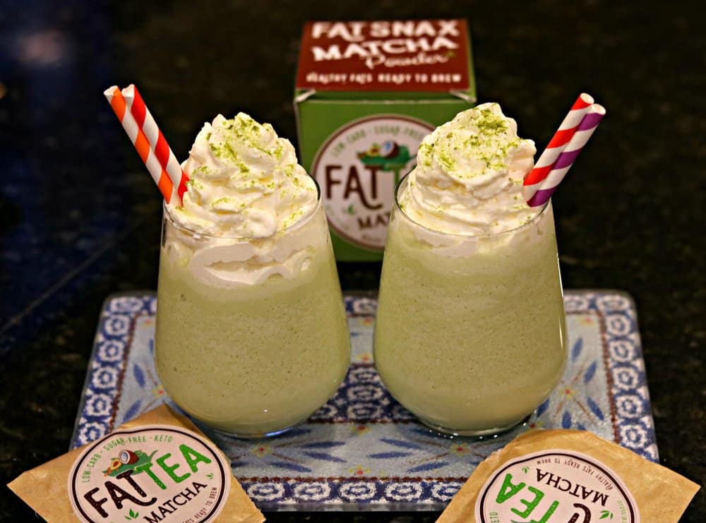 Two glasses of Keto Matcha (Green Tea) Creme Frappuccinos with red and white straws, and surrounded by Fat Snax products