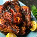 Air Fryer Whole Chicken on a blue serving dish with two lemon halves.