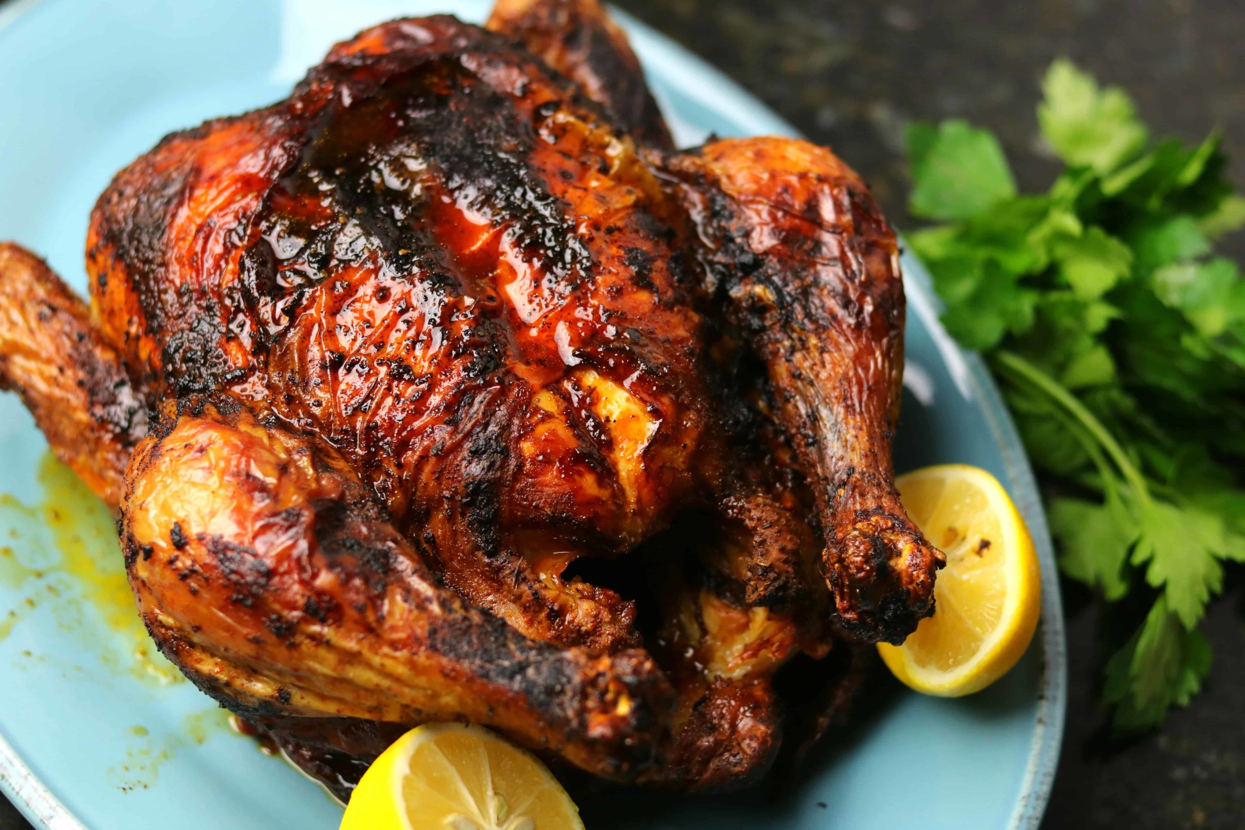 Air Fryer Whole Chicken on a blue serving dish with two lemon halves.