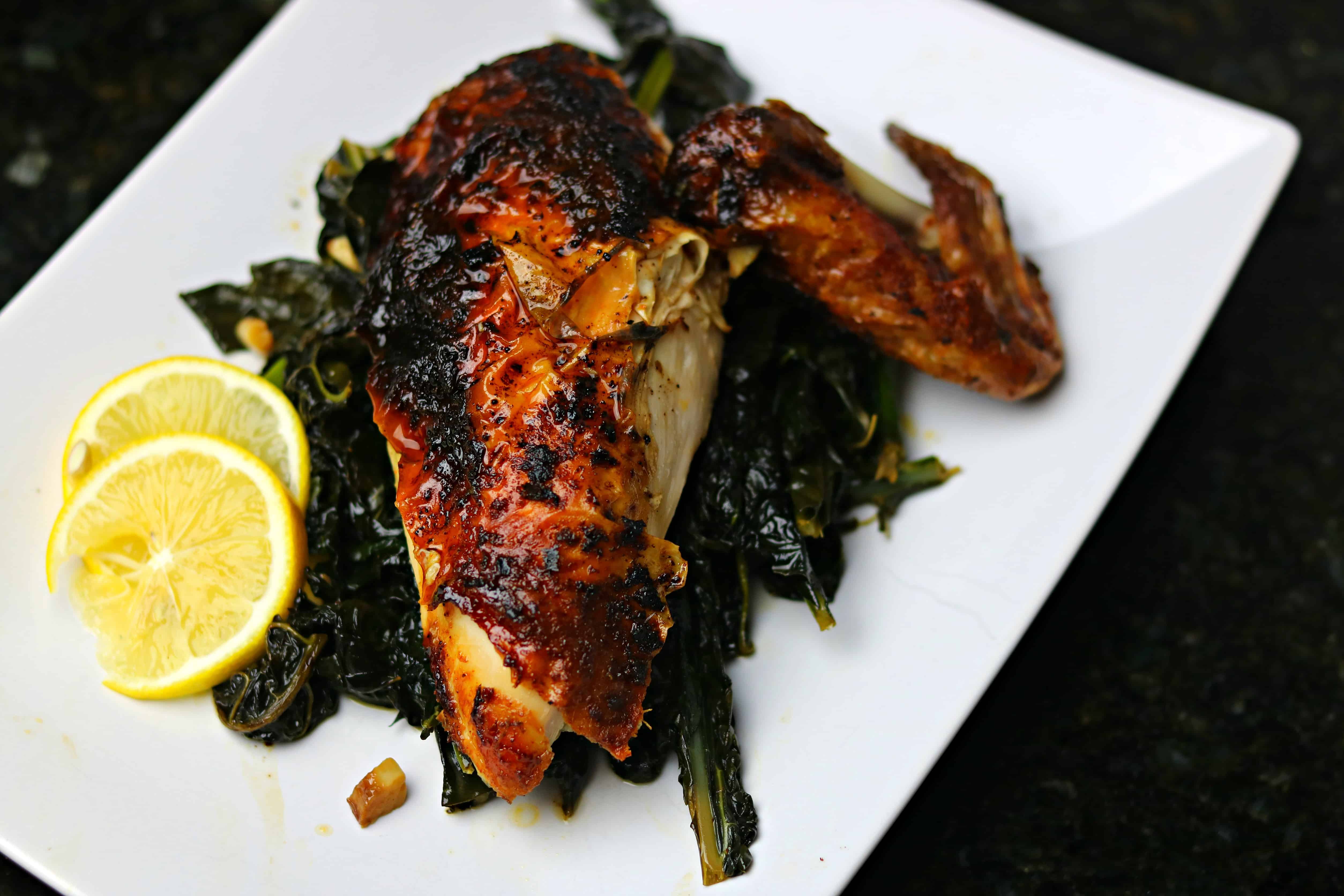 Air Fryer Chicken breast and wing on a bed of collard greens with slices of lemon on a white plate