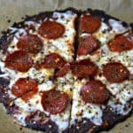 A close-up of keto pepperoni pizza made using Cali'flour Foods cauliflower pizza crusts on parchment paper
