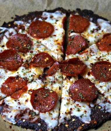 A close-up of keto pepperoni pizza made using Cali'flour Foods cauliflower pizza crusts on parchment paper