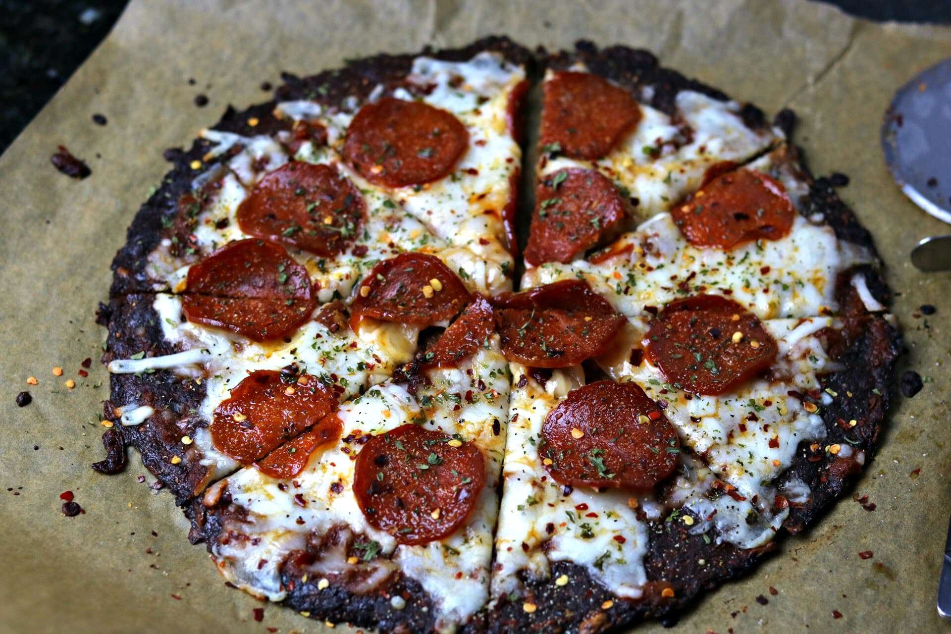 A close-up of keto pepperoni pizza made using Cali\'flour Foods cauliflower pizza crusts on parchment paper