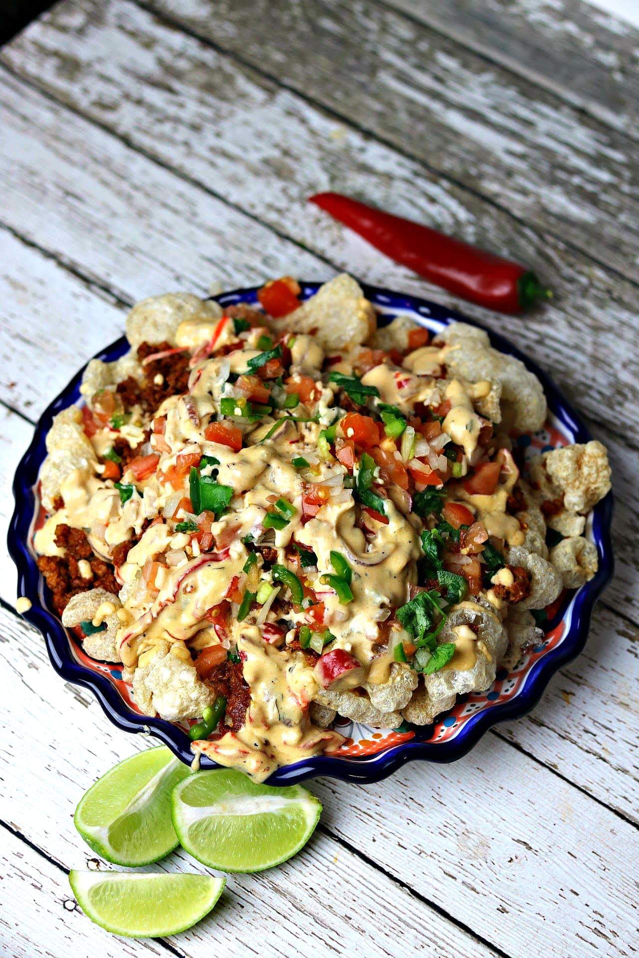 A plate of keto nachos that includes pork rinds, ground chorizo, Pico De Gallo and cheese sauce