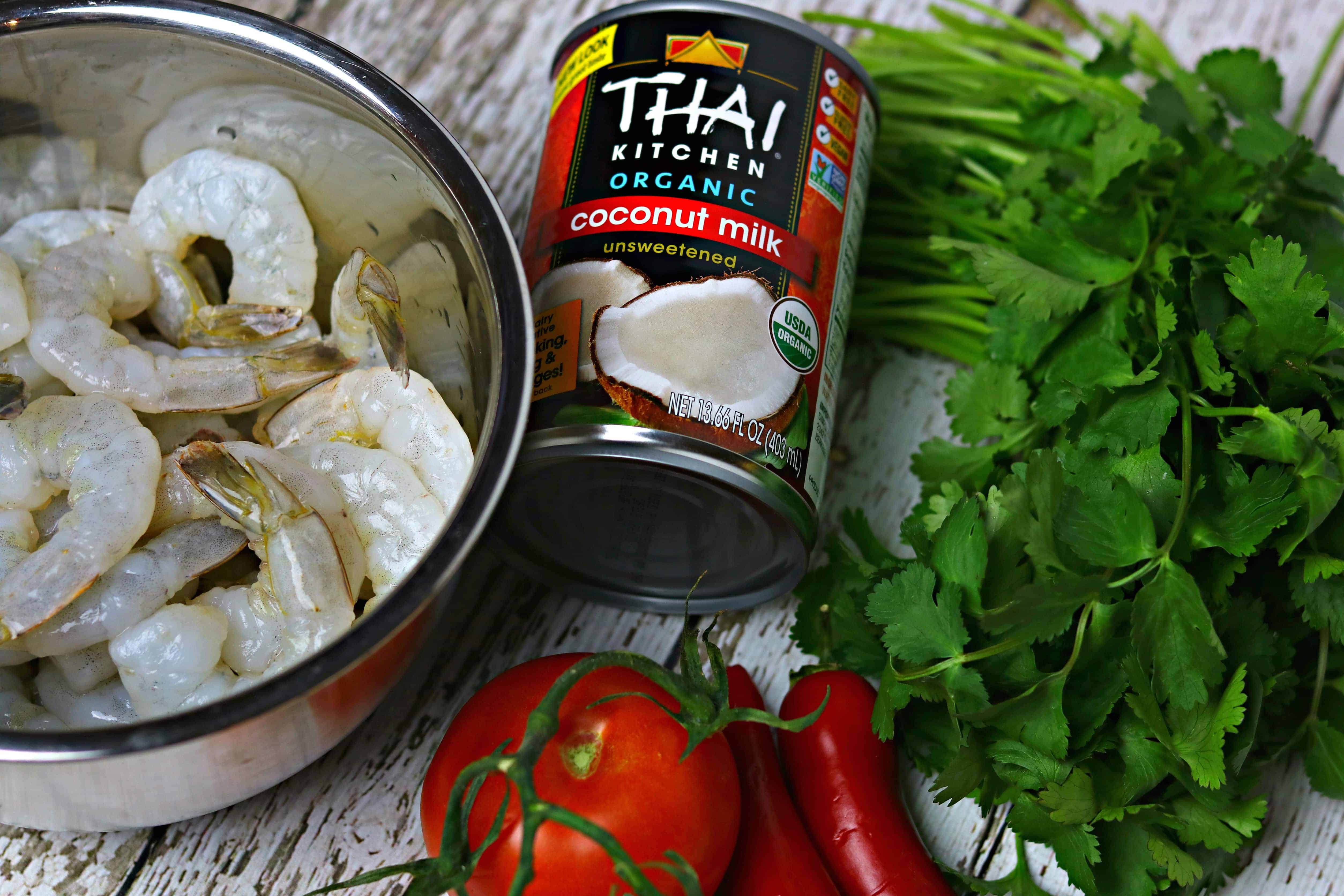 A can of Thai Kitchen Coconut Milk with a metal bowl of raw shrimp, and assorted vegetables