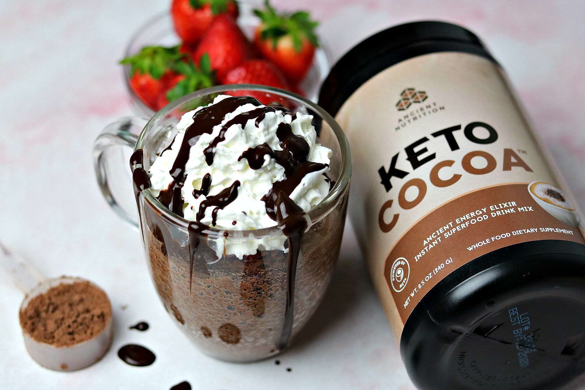 A Keto Chocolate Mug Cake in a glass mug sitting next to a tub of Ancient Nutrition Keto Cocoa