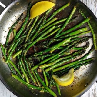 Sauteed asparagus in a frying pan with slices of lemon.