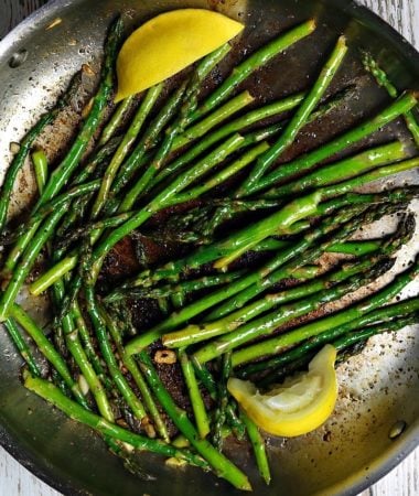 Sauteed asparagus in a frying pan with slices of lemon.