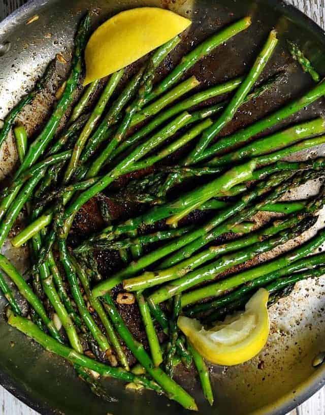 Sauteed asparagus in a frying pan with slices of lemon.