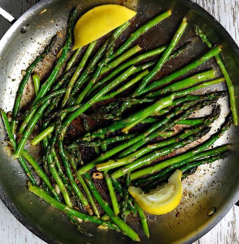 Sauteed asparagus in a frying pan with slices of lemon.