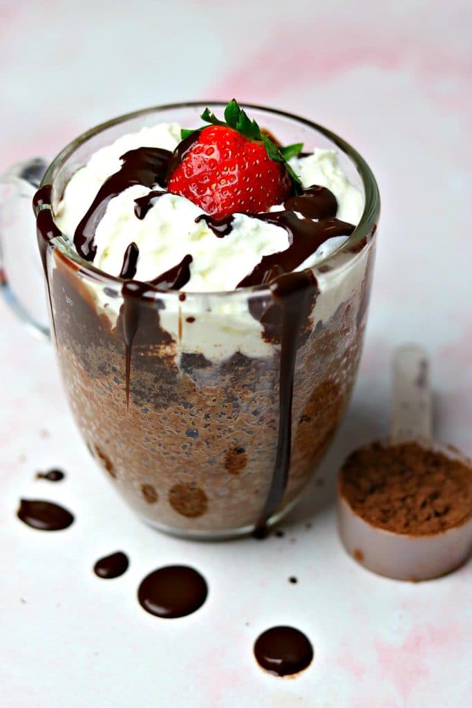 A keto chocolate mug cake in a glass mug topped with whipped cream, chocolate syrup and a strawberry