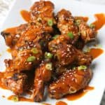 Red Curry Chicken wings on a plate topped with sesame seeds and sliced green onions