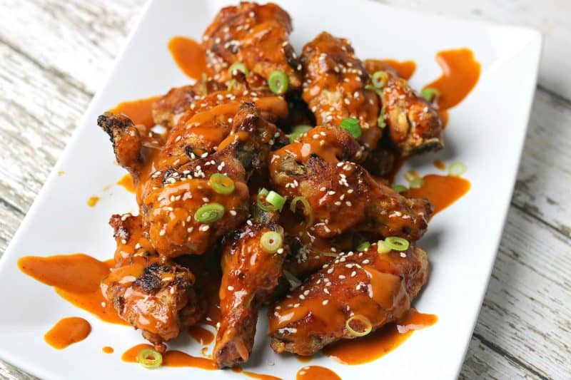 Red Curry Chicken wings on a plate topped with sesame seeds and sliced green onions