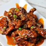 Keto Thai Red Curry Chicken Wings, topped with sesame seeds and green onions, on a white serving dish.