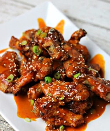 Keto Thai Red Curry Chicken Wings, topped with sesame seeds and green onions, on a white serving dish.