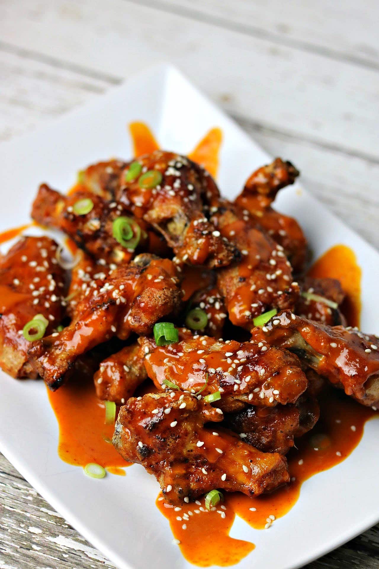 Keto Thai Red Curry Chicken Wings, topped with sesame seeds and green onions, on a white serving dish.