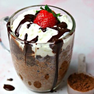 keto chocolate mug cake in a glass mug with a scoop of chocolate powder