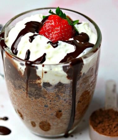 keto chocolate mug cake in a glass mug with a scoop of chocolate powder