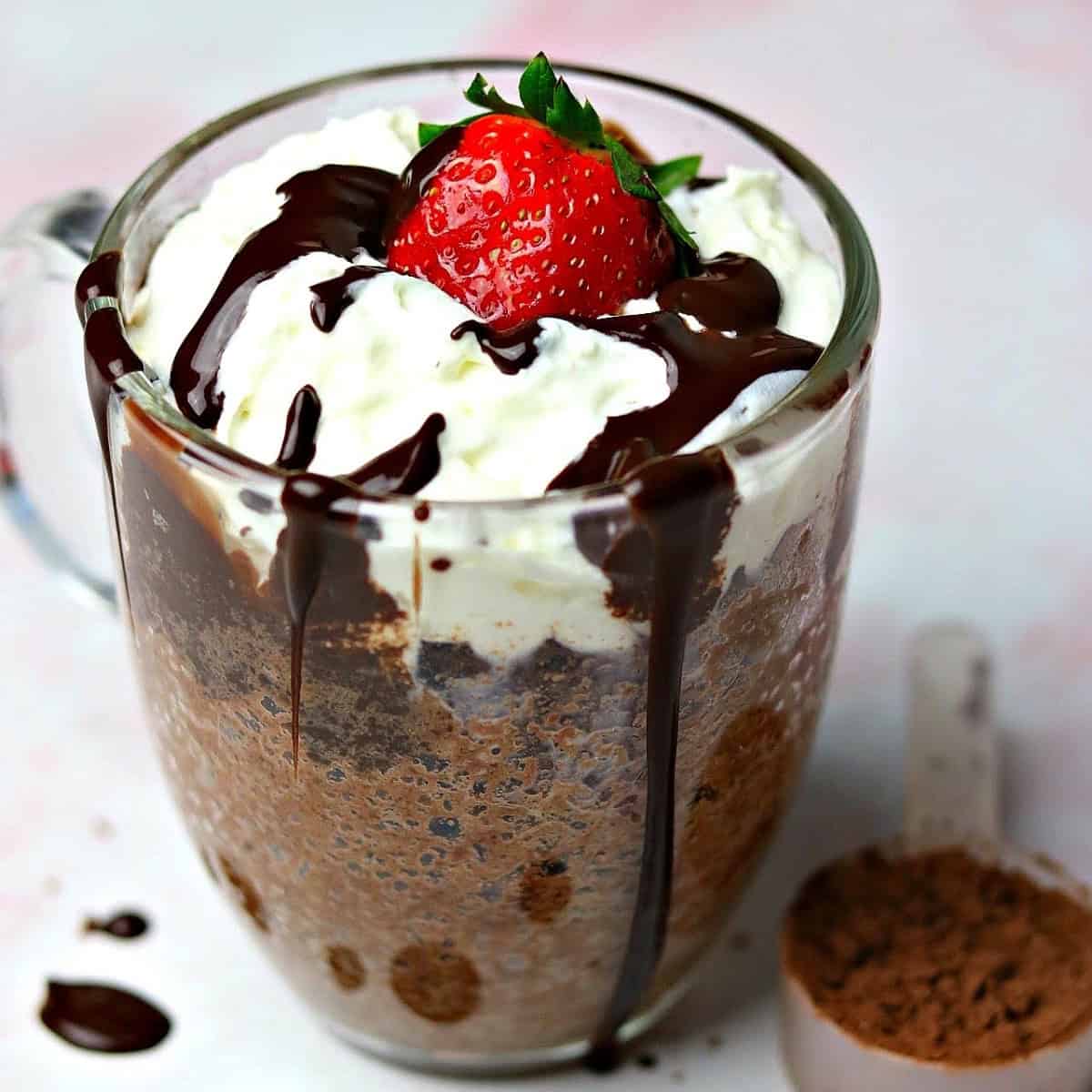 keto chocolate mug cake in a glass mug with a scoop of chocolate powder