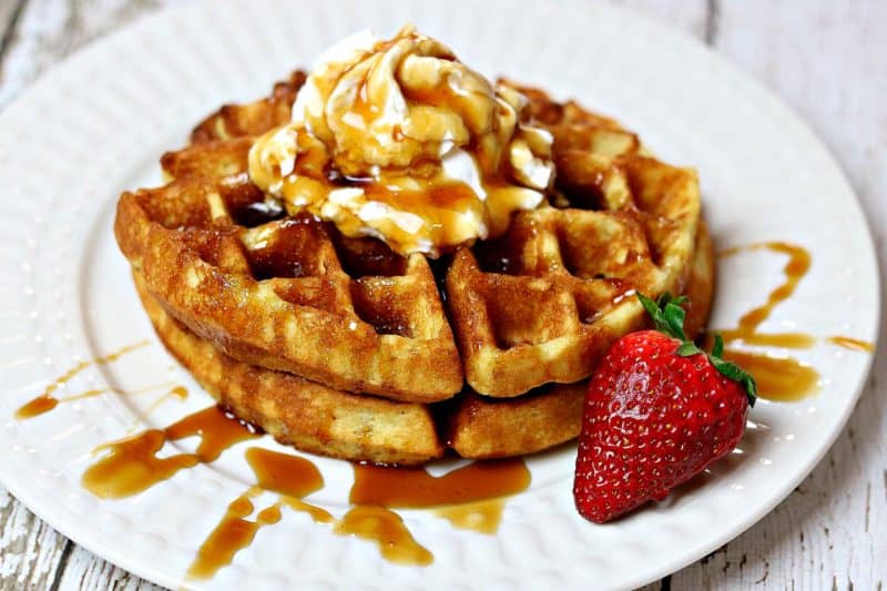 Two gluten-free Belgium waffles on a plate topped with syrup