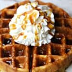 A close up of almond flour waffles on a plate topped with whipped cream and sugar-free maple syrup