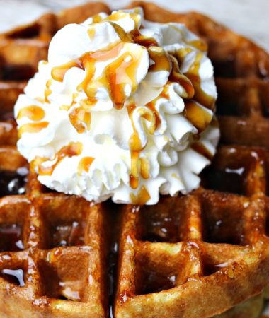 A close up of almond flour waffles on a plate topped with whipped cream and sugar-free maple syrup