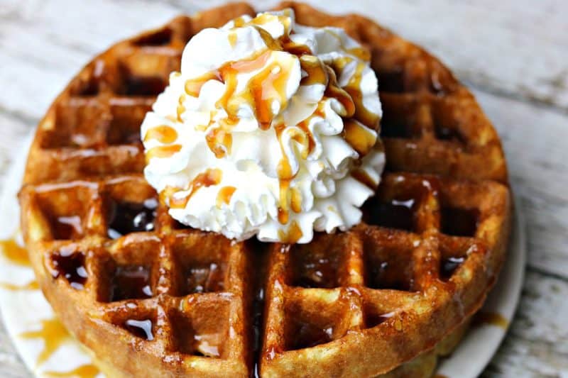 A close up of almond flour waffles on a plate topped with whipped cream and sugar-free maple syrup