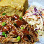 a close-up of Keto BBQ Pulled Pork on a plate with corn-free bread and keto coleslaw