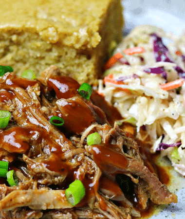 a close-up of Keto BBQ Pulled Pork on a plate with corn-free bread and keto coleslaw