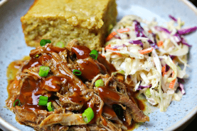 a close-up of Keto BBQ Pulled Pork on a plate with corn-free bread and keto coleslaw