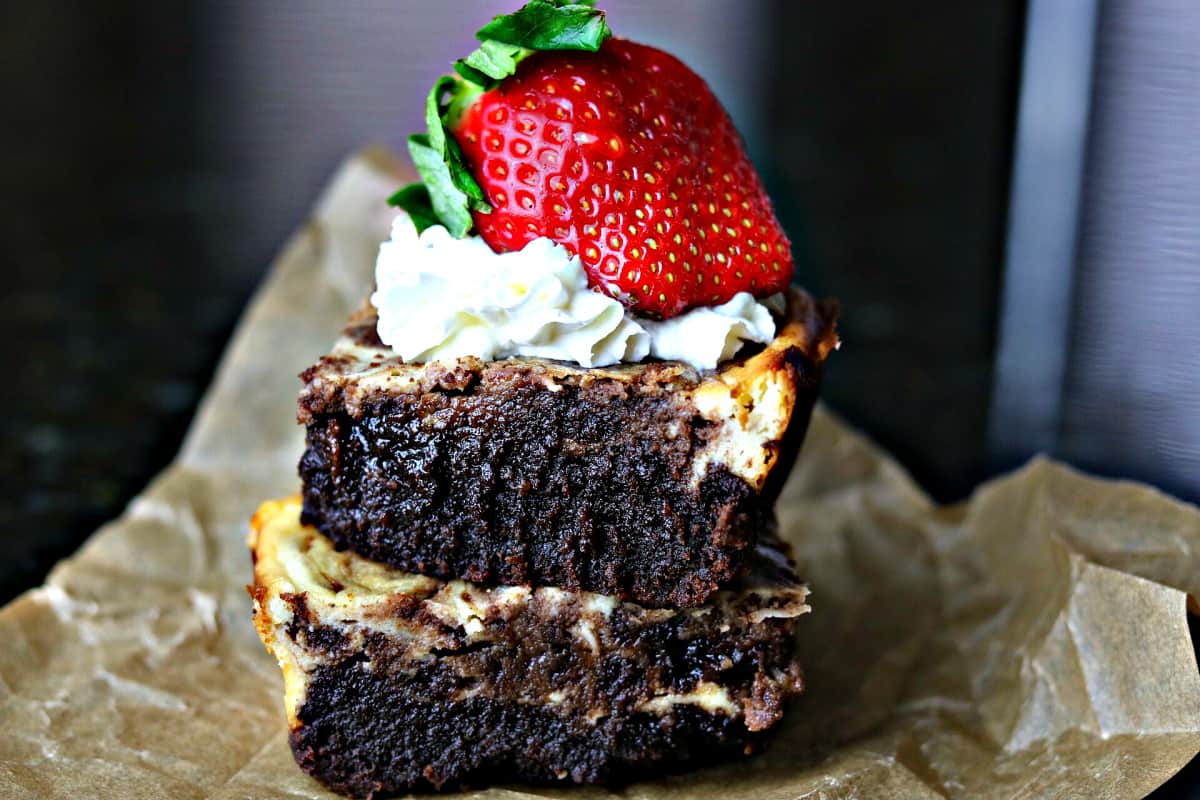 two keto cheesecake brownies stacked on top of each other with whipped cream and strawberries