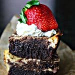 two cheesecake brownies stacked on top of each other with whipped cream and a strawberry