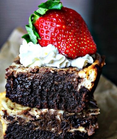 two cheesecake brownies stacked on top of each other with whipped cream and a strawberry