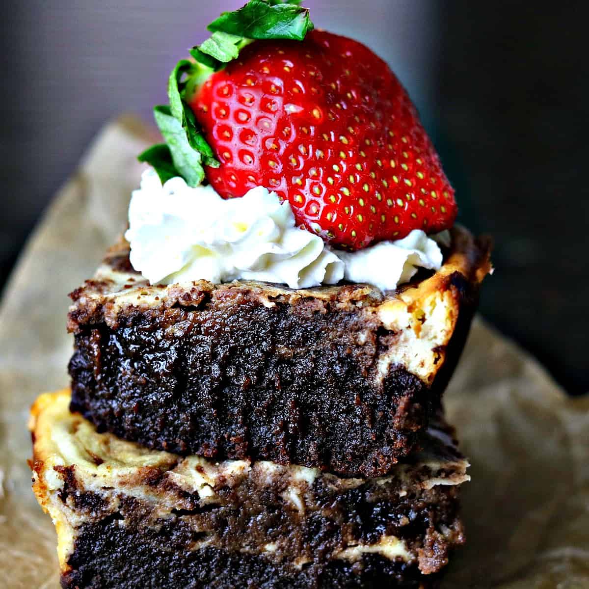 two cheesecake brownies stacked on top of each other with whipped cream and a strawberry
