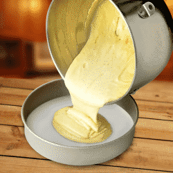 a lifestyle photo showing cake batter being poured into a cake pan lined with parchment paper.