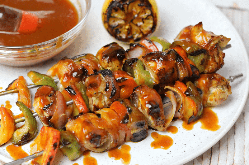 a close-up of Keto Bacon Wrapped Grilled BBQ Chicken Kabobs on a plate with a grilled lemon
