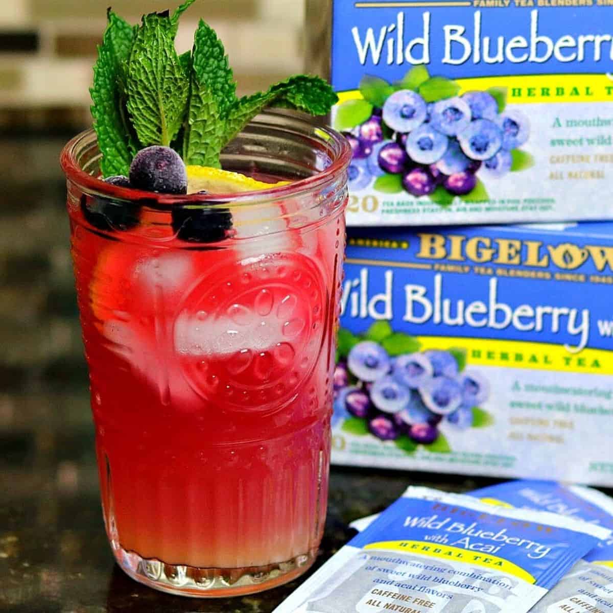 cup of keto blueberry iced tea lemonade with blueberry tea bags in the back