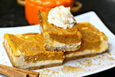 A stack of Keto Pumpkin Pie Cheesecake Bars on a white serving dish