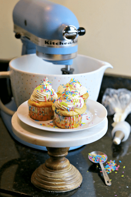 three Keto cupcakes on a stand with a KitchenAid stand mixer