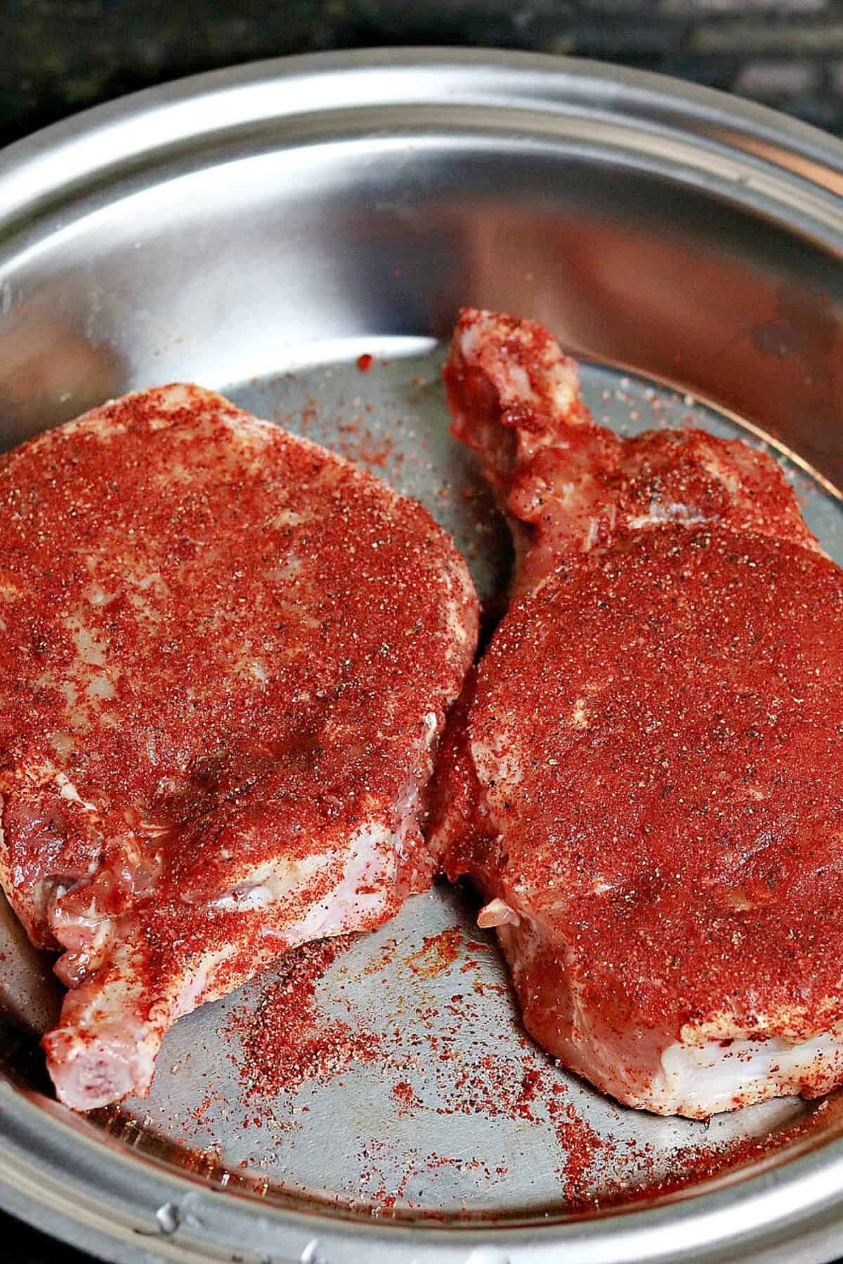 two uncooked bone-in pork chops with seasoning on top