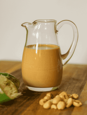 A pitcher of Creamy Thai Peanut Dressing with peanuts in foreground