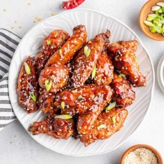 asian sticky wings on a plate with sesame seeds and green onions on the side