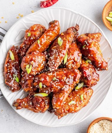 asian sticky wings on a plate with sesame seeds and green onions on the side