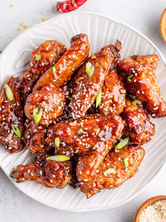 asian sticky wings on a plate with sesame seeds and green onions on the side