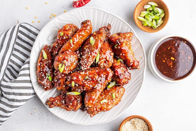 keto sweet chili wings on a plate with green onions, sweet chili sauce, and sesame seeds on the side