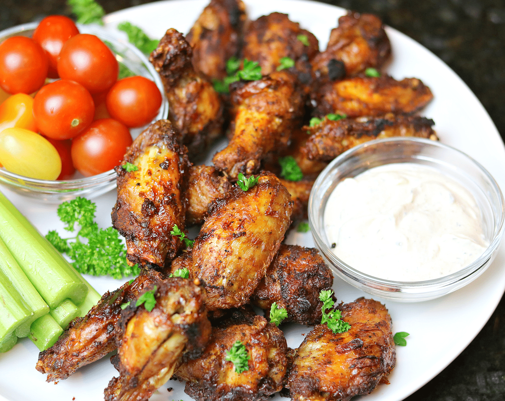 Dry Rub Chicken Wings on a plate with ranch dressing, tomatoes, and celery.