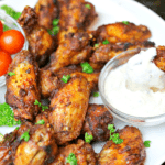 Dry Rub Chicken Wings on a white plate, and one wing being dipped in ranch dressing.